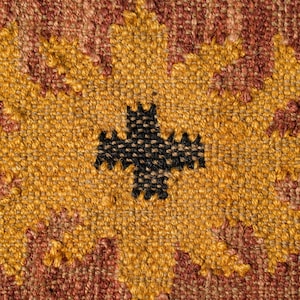 May include: Close-up of a woven fabric with a yellow and brown pattern. The pattern features a large, stylized flower with a black cross in the center.