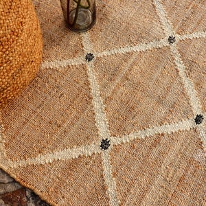 Puede incluir: Primer plano de una alfombra de fibra natural con un patr&oacute;n de diamante tejido en un color m&aacute;s claro. La alfombra tiene acentos negros en todo el dise&ntilde;o.