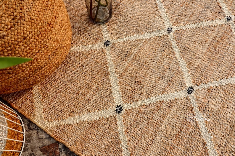 Puede incluir: Primer plano de una alfombra de fibra natural con un patr&oacute;n de diamante tejido en un color m&aacute;s claro. La alfombra tiene acentos negros en todo el dise&ntilde;o.