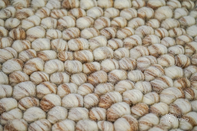 K&ouml;nnte beinhalten: Nahaufnahme eines runden, beige-braunen Wollteppichs aus kleinen, runden Kugeln. Der Teppich hat eine strukturierte, flauschige Oberfl&auml;che.
