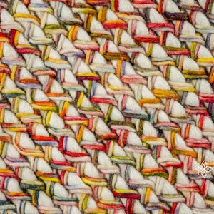 May include: A thick, hand-woven textile featuring a dense, braided pattern of cream-colored yarn interlaced with multicolored strands in shades of red, yellow, green, and blue. The surface displays a repeating diagonal weave with the text INDIA LIVING.