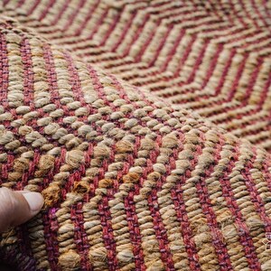 May include: Close-up of a woven rug with a chevron pattern in shades of brown and pink.