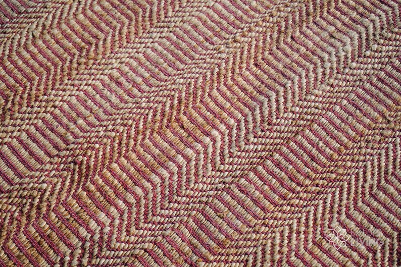 May include: Close-up of a woven rug with a pink and beige chevron pattern.