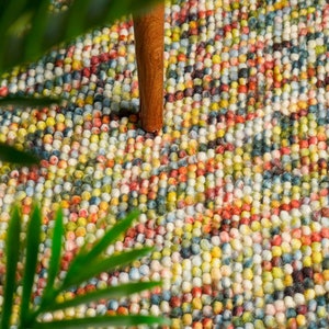 May include: A colourful round rug made of small, densely packed balls of yarn. The rug is a mix of bright colours, including red, yellow, blue, green, and white.