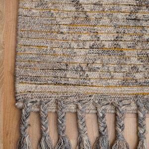 May include: A woven rug with a gray and yellow geometric pattern and braided fringe. The rug is made of natural fibers and has a rustic, hand-crafted look.