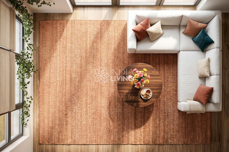 May include: A large rectangular area rug in a warm terracotta orange hue with a textured weave. The rug is positioned under a white L-shaped sectional sofa, a round dark wood coffee table, a floral bouquet, and a small plate with snacks.