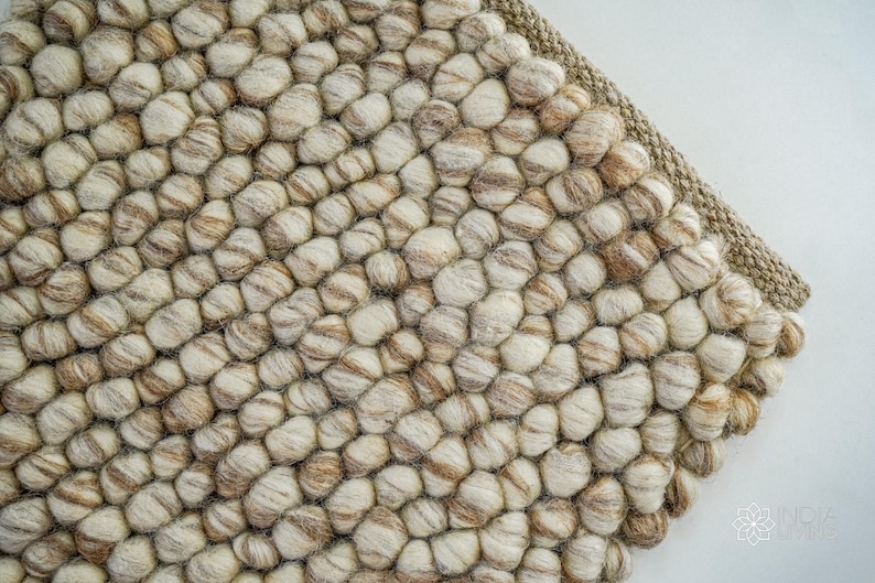 K&ouml;nnte beinhalten: Nahaufnahme eines beige-braunen Wollteppichs mit einer strukturierten, unebenen Oberfl&auml;che. Der Teppich besteht aus kleinen, runden Wollkugeln, die miteinander verwoben sind.