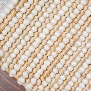 May include: A close-up of a woven rug with a textured surface. The rug is made of natural fibers and has a striped pattern in shades of beige and white.