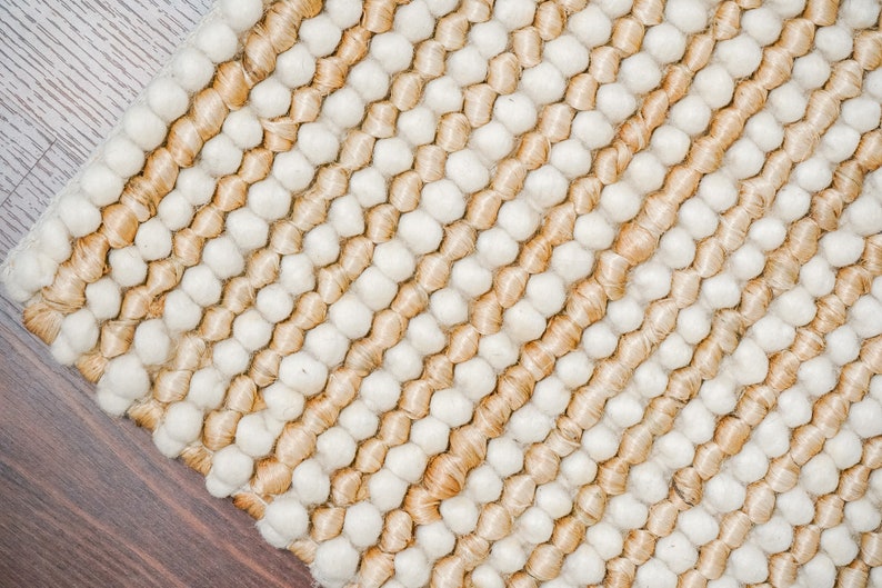 May include: A close-up of a woven rug with a textured surface. The rug is made of natural fibers and has a striped pattern in shades of beige and white.