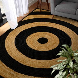 May include: A round jute rug with black and natural colored stripes in a concentric circle pattern. The rug is made of natural fibers and has a rustic look.
