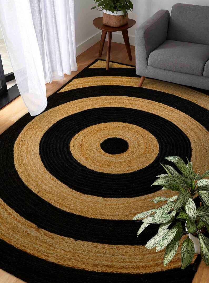 May include: A round jute rug with black and natural colored stripes in a concentric circle pattern. The rug is made of natural fibers and has a rustic look.