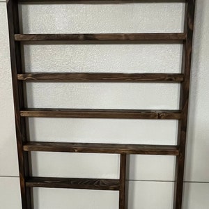 May include: A dark brown wooden wall shelf with five shelves and a small cubby on the bottom right. The shelf is mounted on a white wall.