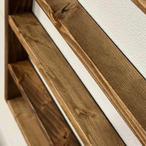 May include: A wooden shelf unit with three shelves stained in a walnut color. The shelves are angled and the wood grain is visible. The text "Walnut Stain" is visible at the bottom of the image.