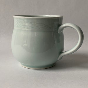 Puede incluir: Una taza de cerámica azul claro con un diseño ondulado alrededor del borde.