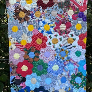 May include: A handmade quilt featuring a floral design. The quilt is composed of numerous hexagonal fabric pieces, arranged to form flower shapes. The flowers are in various colors, including red, yellow, blue, and green, with a mix of patterned fabrics.