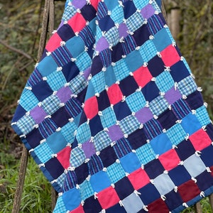 May include: A patchwork quilt made from squares of blue, pink, purple, and white fabric. The quilt is tied with white yarn and has a frayed edge.