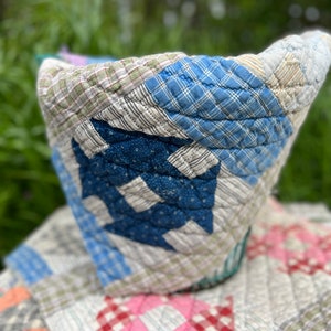 May include: A patchwork quilt made of various blue, green, and pink plaid fabrics. The quilt is folded in a bowl shape and is sitting on top of another quilt with a pink and red checkered pattern.