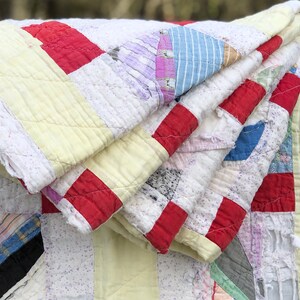 May include: A vintage quilt made from scraps of fabric in various colors and patterns, including red, white, blue, yellow, and purple. The quilt is folded and layered, showing the different fabrics and stitching.