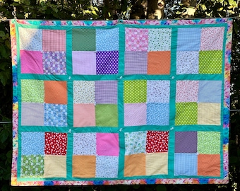 May include: A patchwork quilt with a variety of colorful floral and geometric patterns. The quilt is made up of 25 squares, each with a different design. The quilt is hanging on a clothesline.
