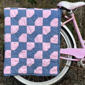 May include: A pink and blue patchwork quilt with a ruffled edge is draped over the back wheel of a pink bicycle.