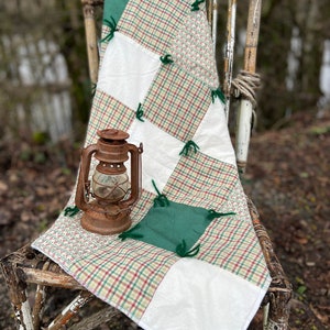 May include: A green, white, and brown patchwork quilt with tied knots is draped over a wooden chair. An antique lantern sits on the quilt.