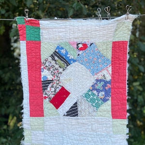 May include: A vintage quilt with a patchwork design featuring a variety of floral and geometric patterns in shades of red, blue, green, and white. The quilt is hanging on a clothesline with clothespins.