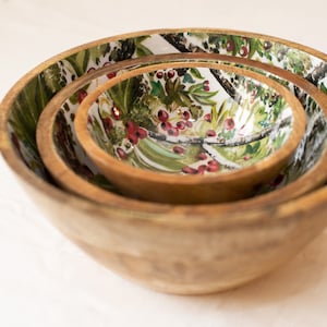 May include: Set of three wooden bowls with a floral design featuring green leaves, white branches, and red berries.