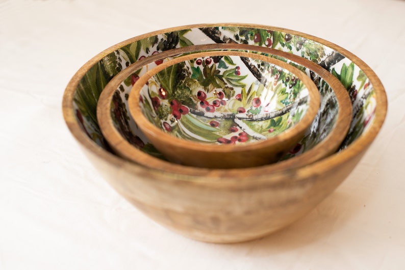 May include: Set of three wooden bowls with a floral design featuring green leaves, white branches, and red berries.