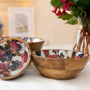 May include: Three wooden bowls with a white background and a colorful berry pattern. The bowls are made of natural wood and have a rustic look.