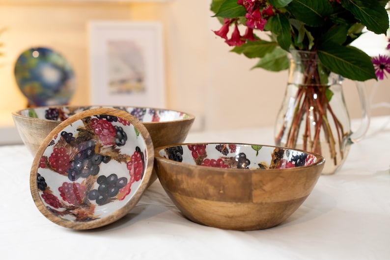 May include: Three wooden bowls with a white background and a colorful berry pattern. The bowls are made of natural wood and have a rustic look.