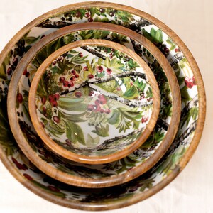 May include: Set of three nesting bowls with a white background and a floral pattern featuring green leaves, white branches, and red berries.
