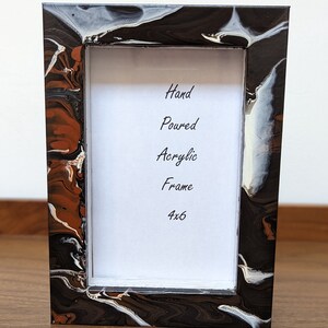 May include: A hand-poured acrylic picture frame with a black, white, and brown marbled design. The frame is 4x6 inches.