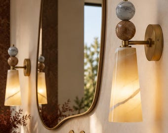 Peut inclure: Une applique murale composée d'un abat-jour conique en verre ambré surmonté d'un design à sphères empilées en marbre brun et blanc, avec une base et un bras en métal doré, éclairant un espace de lavabo de salle de bain.