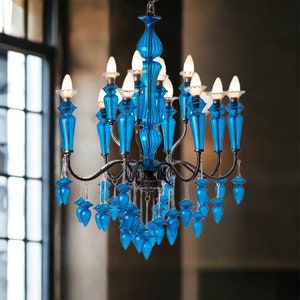 May include: A vibrant blue chandelier with multiple light fixtures. The chandelier features ornate, teardrop-shaped glass elements and a dark metal frame. The lights are illuminated, casting a warm glow. The design is elegant and decorative, suitable for interior decor.