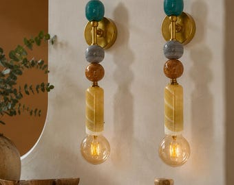 Peut inclure: Deux appliques murales composées d'un empilement vertical de perles bleu sarcelle, grises et ambrées, fixées sur un support en laiton. Chaque luminaire présente un élément cylindrique en verre jaune et une ampoule ronde de style Edison.