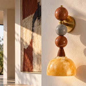 May include: A wall sconce featuring a brass mounting plate, two stacked reddish-brown marble spheres, one grey marble sphere, and a ribbed brown connector piece above a translucent, dome-shaped yellow alabaster glass shade.