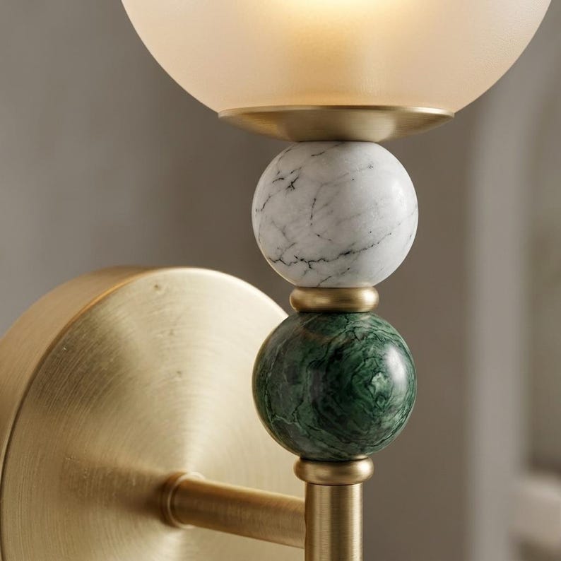 May include: Close-up of a wall sconce with a frosted glass globe shade. The sconce features a brass finish and decorative spheres of white marble and green marble. The fixture is designed for indoor lighting.