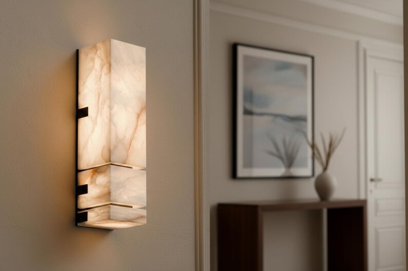 Op de afbeelding: Een moderne wandlamp met een rechthoekig, gelaagd ontwerp. De lamp is gemaakt van een doorschijnend, cr&egrave;mekleurig materiaal met bruine adering, gemonteerd op een zwart metalen frame. De lamp is verlicht en geeft een warme gloed.