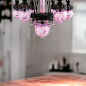 May include: Ornate chandelier with a black metal frame and pink glass shades. The chandelier has a central column and curved arms, each holding a pink glass globe. Decorative crystals hang from the bottom.