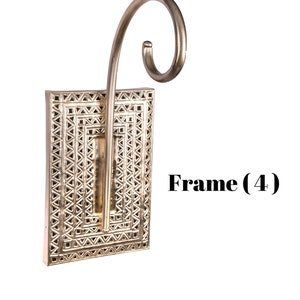 May include: A silver-colored wall sconce with a rectangular frame featuring a geometric design. The sconce has a curved, decorative arm extending upwards. The text "Frame (4)" is visible on the right side.