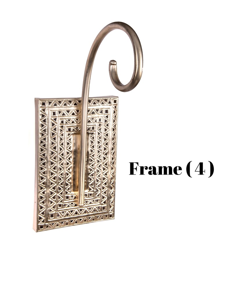 May include: A silver-colored wall sconce with a rectangular frame featuring a geometric design. The sconce has a curved, decorative arm extending upwards. The text "Frame (4)" is visible on the right side.
