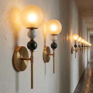 May include: A series of wall sconces with a modern design. Each sconce features a round, frosted glass globe, marble and green stone accents, and a brass finish. The sconces are mounted on a textured white wall, creating a warm, inviting ambiance.