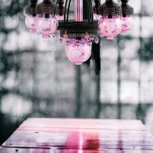 May include: A decorative chandelier with a black metal frame and pink glass globes. The chandelier hangs above a wooden table, creating a soft, romantic ambiance. The pink glass is accented with dangling pink beads.