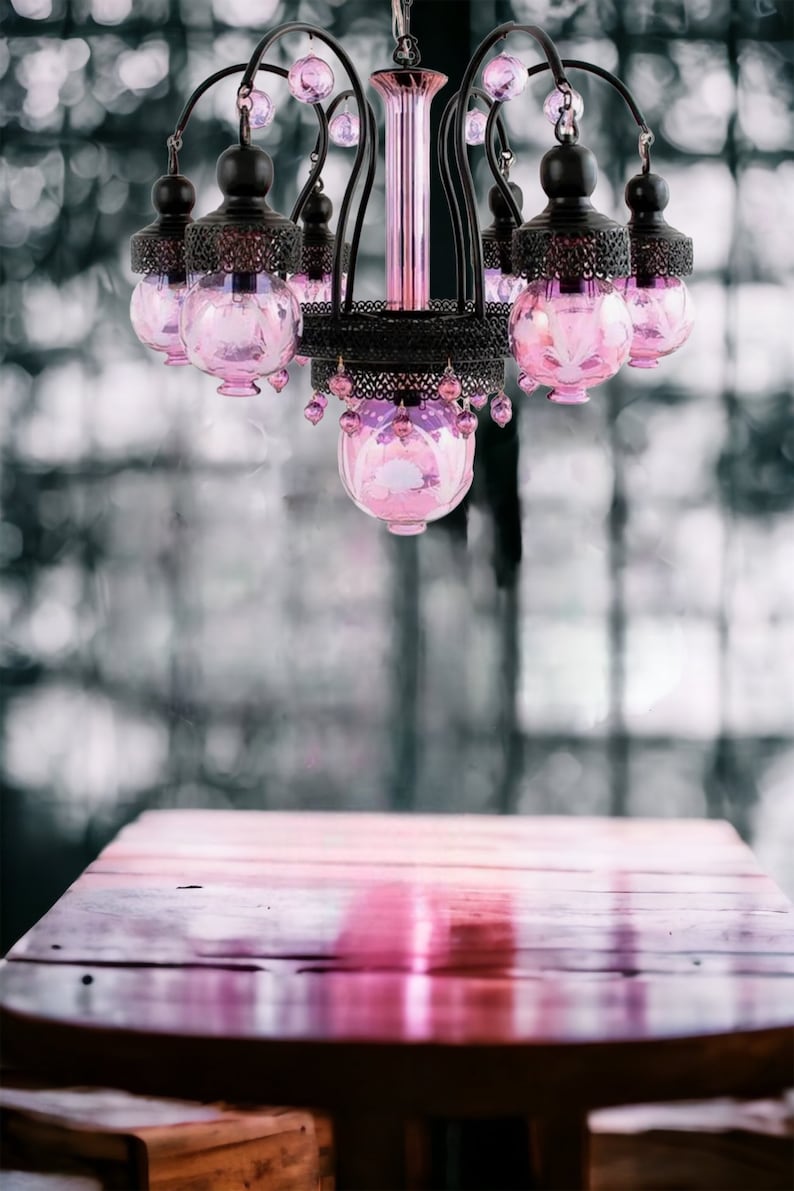 May include: A decorative chandelier with a black metal frame and pink glass globes. The chandelier hangs above a wooden table, creating a soft, romantic ambiance. The pink glass is accented with dangling pink beads.
