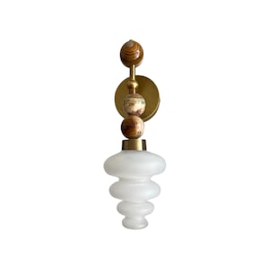 May include: A wall-mounted light fixture with a brass finish and a frosted glass shade. The sconce features decorative stone spheres in brown and green. The light is designed for indoor use and adds a touch of elegance. The overall height is approximately 30 cm.