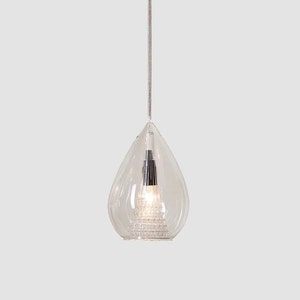 May include: A clear, teardrop-shaped pendant light fixture. The glass shade has a textured, tiered base and a silver-colored interior. A thin, silver cord suspends the light from above, creating a modern and elegant design.