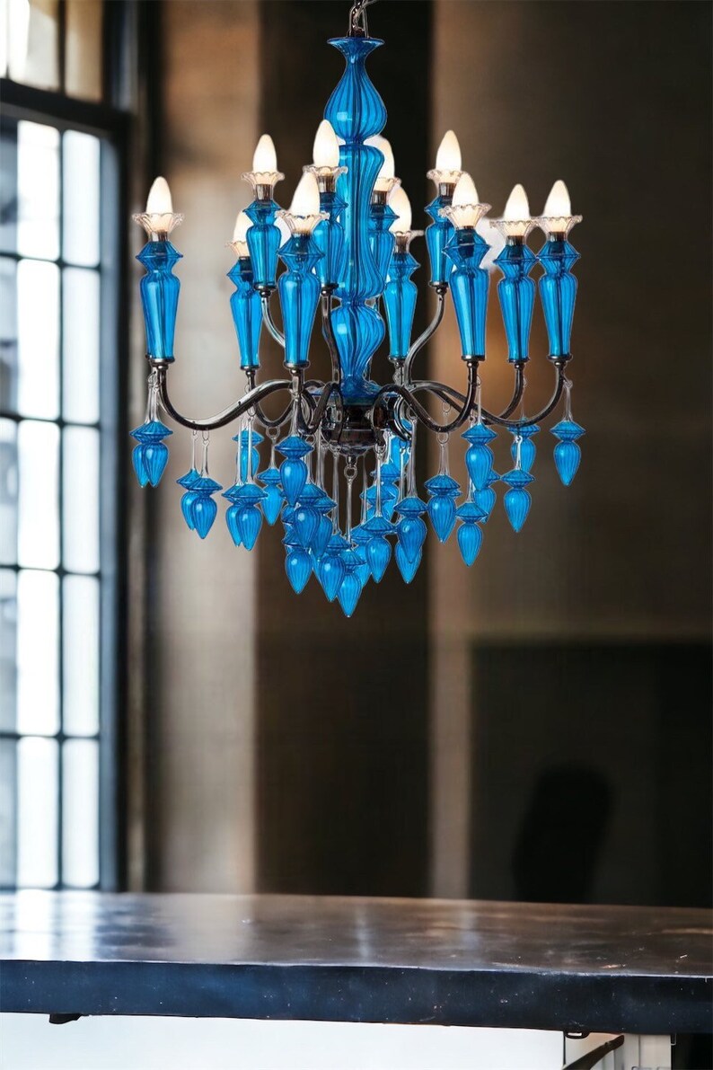 May include: A vibrant blue chandelier with multiple light fixtures. The chandelier features ornate, teardrop-shaped glass elements and a dark metal frame. The lights are illuminated, casting a warm glow. The design is elegant and decorative, suitable for interior decor.