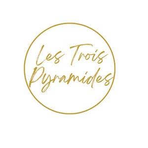 May include: A gold-colored logo featuring the words "Les Trois Pyramides" in a cursive font, enclosed within a gold circle. The background is plain white.