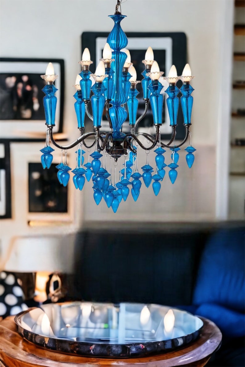 May include: A vibrant blue chandelier with multiple light bulbs. The chandelier has a decorative design with blue glass elements and a silver metal frame. The fixture hangs in a room with framed artwork.