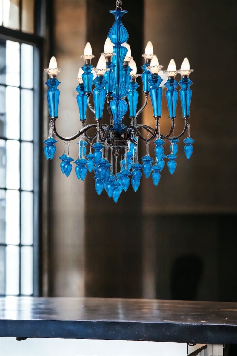 May include: A vibrant blue chandelier with multiple lights and decorative glass elements. The chandelier has a dark metal frame and is suspended above a dark surface. The glass elements are a bright, eye-catching blue.